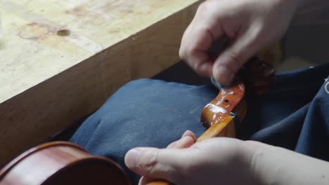 master-artisan-luthier-violin-maker-antiquize-violin-curl-and-peg-box-with-cloth-and-acid-caustic-oil-on-new-stringed-instrument-to-reproduce-original-masterpiece-distress