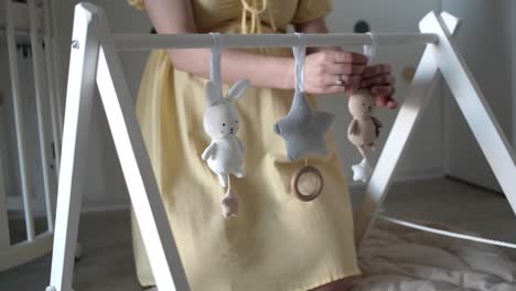 Pregnant-woman-hanging-stuffed-animal-toys-on-baby-play-gym-made-of-wood-in-nursery