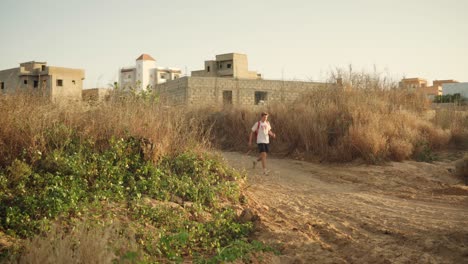 White-Man-Walks-Down-Dirt-Track-in-Senegal,-Africa
