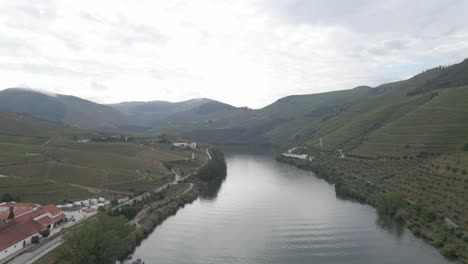 Aerial-view-of-the-wine-town-of-Pinhão-Portugal-,-Drone-moving-forward-over-the-river-Douro-showing-the-vines-plantations-and-the-mountains-in-the-background