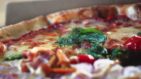 Primer-Plano-De-Una-Sabrosa-Pizza-Italiana-Con-Salsa-De-Pesto-En-Una-Caja-De-Pizza-De-Cartón-Sobre-La-Mesa,-Tiro-Giratorio