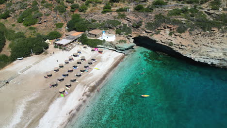 Aerial-drone-video-from-iconic-sandy-beach-of-Andros-with-sun-beds-and-umbrellas,-Cyclades,-Greece