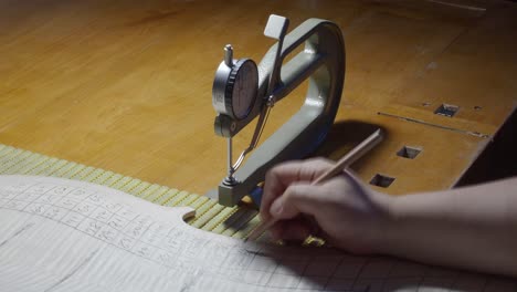 Stringed-instrument-maker-master-luthier-proceed-with-graduation-work-in-cello-back-plate,-use-thickness-gauge-caliper,-measure-levels,-use-pencil-write-values-on-wood-,-Cremona,-Italy-workshop