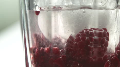 Close-up-of-a-glass-with-effervescent-water-and-fresh-raspberries,-the-bubbles-clinging-to-the-fruit,-creating-a-refreshing-and-appealing-visual-beverage
