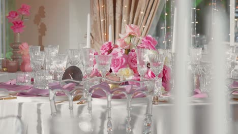 Shot-of-fancy-wedding-reception-table-with-glasses-and-plates,-table-is-decorated-with-gorgeous-pink-and-white-roses-and-white-candles,-panning-shot