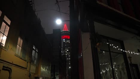 View-of-Vancouver-lookout-tower-glowing-red-in-the-distance-from-a-view-down-a-dark-and-dangerous-alleyway-side-street-littered-with-trash-at-night