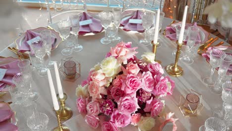 Shot-of-fancy-wedding-reception-table-with-glasses-and-plates,-table-is-decorated-with-gorgeous-pink-and-white-roses-and-white-candles,-close-up-shot