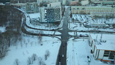 Aerial-view-of-a-modern-urban-intersection-surrounded-by-snow-covered-trees-and-buildings,-showcasing-the-organized-chaos-of-city-infrastructure-against-the-quiet-of-winter-in-Gdańsk