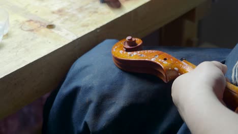 master-artisan-luthier-violin-maker-antiquize-violin-curl-and-peg-box-with-cloth-and-acid-caustic-oil-on-new-stringed-instrument-to-reproduce-original-masterpiece-distress