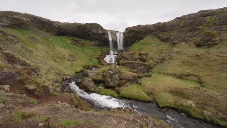 Wasser,-Das-Entlang-Eines-Baches-Fließt,-Der-Von-Einem-Wasserfall-In-Island-Gespeist-Wird