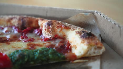 Closeup-shot-of-tasty-Neapolitan-pizza-with-pesto-sauce-in-a-cardboard-pizza-box-on-the-table,-sliding-shot