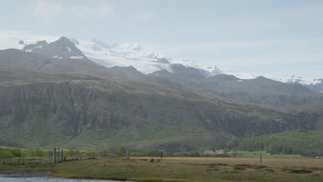 Snow-capped-mountains-in-the-Icelandic-countryside-with-a-lake-and-houses-in-the-foreground