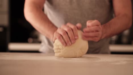 Man-of-the-house-flouring-pizza-dough-on-countertop-in-home-kitchen-and-kneading-it
