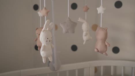 Cute-stuffed-baby-animals-rotating-above-white-wooden-crib-in-nursery