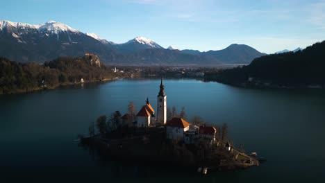 Drone-Descends-to-Reveal-Mountain-Landscape-Behind-Bled-Island,-Slovenia