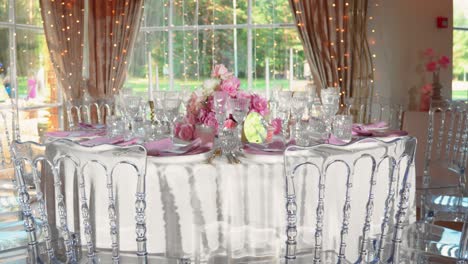 Shot-of-fancy-wedding-reception-table-with-glasses-and-plates,-table-is-decorated-with-gorgeous-pink-and-white-roses-and-white-candles,-zoom-in-shot