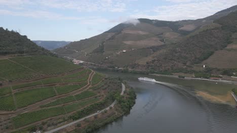 Luftaufnahme-Der-Weinstadt-Pinhão-In-Portugal,-Drohne-Bewegt-Sich-Nach-Rechts-über-Den-Fluss-Douro-Und-Zeigt-Die-Weinplantagen-Und-Ein-Touristenschiff,-Das-Den-Fluss-Hinunterfährt