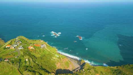 Aerial-flyover-green-hill-with-houses-on-top-and-blue-Atlantic-ocean-on-Madeira-Island