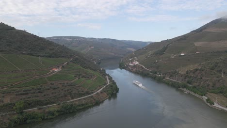 Aerial-view-of-the-wine-town-of-Pinhão-Portugal-,-Drone-moving-to-the-right-over-the-river-Douro-showing-the-vines-plantations-and-a-tourist-ship-going-down-the-river