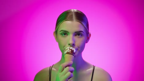 Close-up-shot-Attractive-blonde-young-woman-eating-a-chocolate-dipped-ice-cream-cone-in-a-studio-with-infinite-background