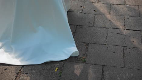 Nahaufnahmen-Des-Schweifs-Eines-Weißen-Hochzeitskleides-Einer-Braut,-Die-Auf-Einem-Betonfliesenpfad-Läuft