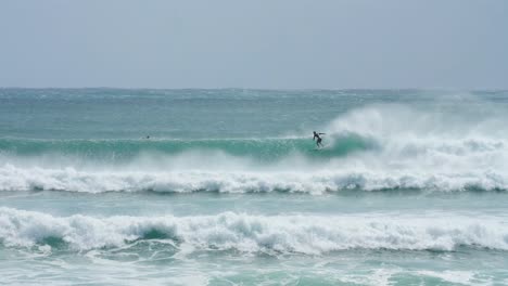 A-surfer-dropping-in-on-a-wave-in-crystal-clear-waters,-with-offshore-wind-in-slow-motion