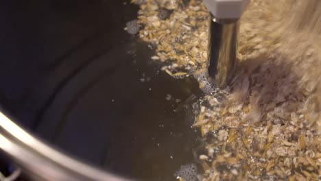 Crushed-malt-is-added-to-hot-water-in-a-stainless-steel-brew-kettle-for-start-of-mashing-process---close-up-view-of-beer-making