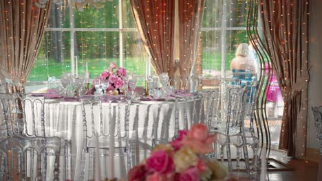 Shot-of-fancy-wedding-reception-tables-with-glasses-and-plates,-table-is-decorated-with-gorgeous-pink-and-white-roses-and-white-candles,-panning-shot