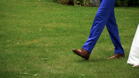 Closeup-shot-of-the-legs-of-bride-and-groom-walking-together-on-the-grass-in-the-park-on-the-sunny-wedding-day,-slow-motion