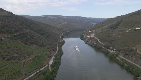 Aerial-view-of-the-wine-town-of-Pinhão-Portugal-,-Drone-moving-forward-over-the-river-Douro-showing-the-vines-plantations-and-a-tourist-ship-going-down-the-river