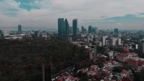 Drone-captured-aerial-view-over-Mexico-City,-highlighting-diverse-architecture,-bustling-traffic,-greenery,-and-a-stunning-backdrop-of-blue-sky-and-clouds