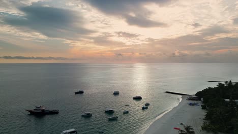 Sunset-and-boats-at-calm-Pacific-Ocean-shore-in-Fulidhoo,-Maldives