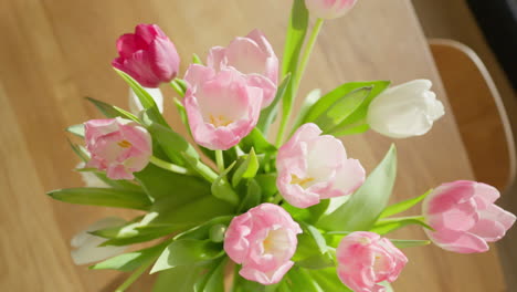 Top-shot-of-delicate-tulips-in-a-vase,-dollying-out-to-reveal-a-warm,-sunlit-wooden-table-setting