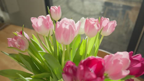 Slow-motion-dolly-in-shot-of-vibrant-tulips-in-a-vase-on-a-rustic-wooden-table,-highlighted-by-a-backlit-sun