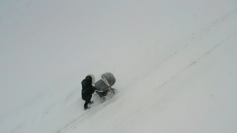 Aerial-view-of-mother-walk-with-baby-carriage-on-snowy-countryside-road