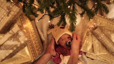Father-placing-newborn-baby-boy-under-the-Christmas-tree