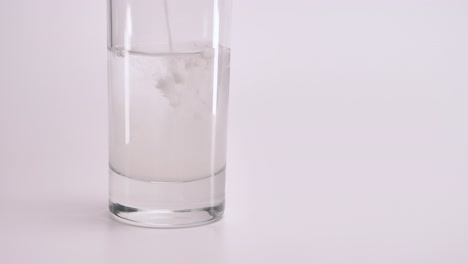 White-medical-powder-is-poured-into-a-glass-of-clean-water-on-a-white-background