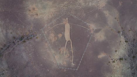 Slow-Pull-Up-and-Away-from-Blythe-Intaglios-in-Arizona-Desert,-Ancient-Geoglyph-in-Center-of-Frame-Surrounded-by-Desert-Terrain