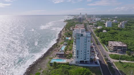 Aerial-orbiting-shot-of-luxury-hotel-area-with-sea-view-on-Caribbean-sea-during-sunny-day-in-Juan-Dolio,-Dominican-Republic---Road-along-coastline-and-sunlight-reflection-on-water-surface---wide-shot