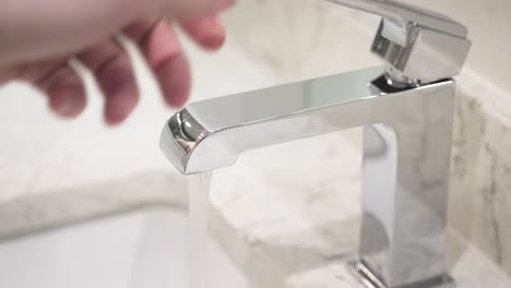 A-person-reaches-into-frame-and-turns-on-the-stylish-silver-faucet-in-slow-motion