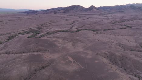 Aerial-Drone-Shot-of-Sonoran-Desert-at-Sunset,-Intaglio-Geoglyphs-Below-and-Mountain-Range-on-the-Horizon