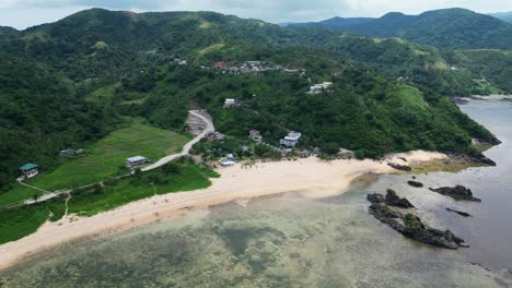Idyllic-aerial-orbit-of-colorful,-tropical-white-sand-beach-resort-with-lush-mountains-and-winding-roads