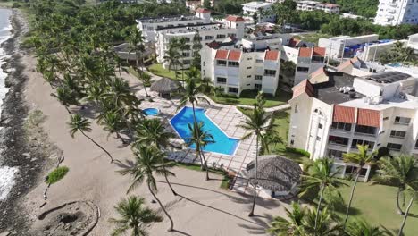 Aerial-birds-eye-shot-of-apartment-hotel-with-swimming-pool-and-palm-trees-during-sunny-day-in-Juan-Dolio,-Dominican-Republic---Top-down-orbit-flight