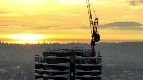 Aerial-View-Of-Tower-Crane-On-High-rise-Building-Under-Construction-At-Sunset-In-Vancouver,-Canada