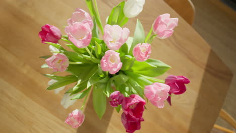 Aerial-top-view-of-vibrant-pink-and-white-tulips-in-a-vase-on-a-wooden-table,-sunlight-enhancing-their-colors
