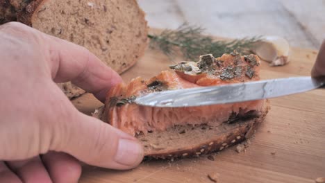 A-man-puts-smoked-salmon-on-a-piece-of-bread-and-adds-a-sprig-of-dill-on-a-wooden-cutting-board
