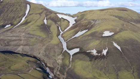 Smooth-aerial-close-up-focus-on-a-green-mountain-with-patches-of-snow-in-Landmannalaugar,-Iceland