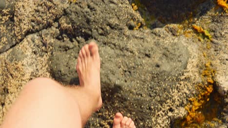 POV-shot-of-man-and-woman-walking-bare-foot-on-rocky-coast-beach,-high-angle