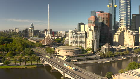 Aerial-view-of-cars-moving-on-a-bridge-over-the-Yarra-River,-with-towering-skyscrapers-in-the-background