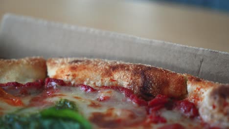 Nahaufnahme-Einer-Leckeren-Neapolitanischen-Pizza-Mit-Pesto-Sauce-In-Einer-Pizzaschachtel-Aus-Pappe-Auf-Dem-Tisch,-Herauszoomen